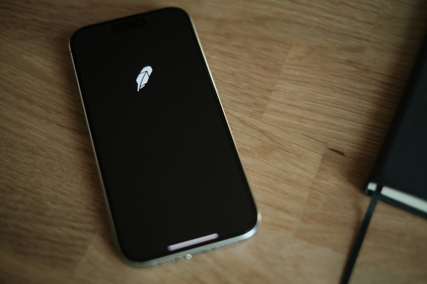 A smartphone displaying a feather logo sits on a wooden desk.
